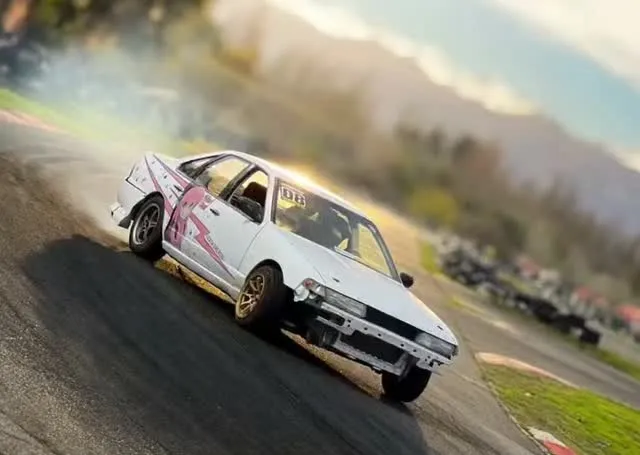 Diego drifting a white car on a race track, tyre smoke behind it